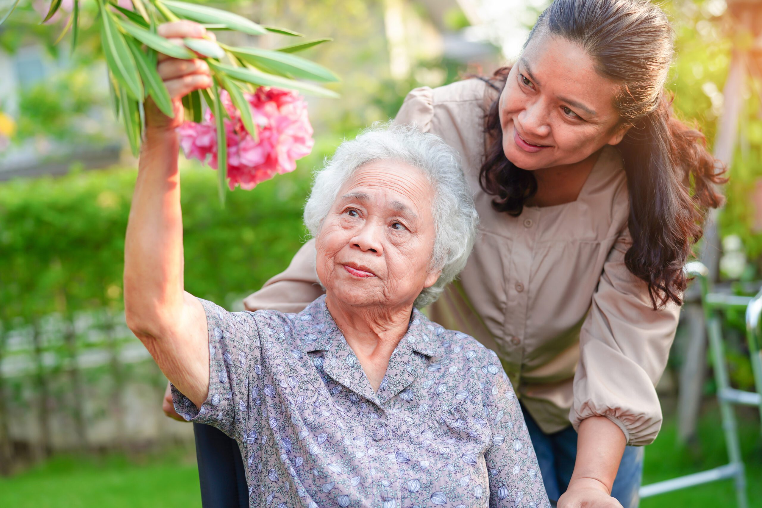 asian-elderly-woman-enjoy-flower-garden-with-caregiver-outside